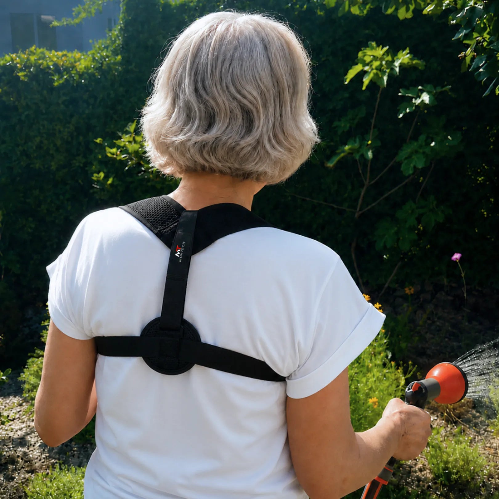 Idős hölgy Movtech BACKO tartásjavítót visel a kertben, hátulnézetben a háti pánttal