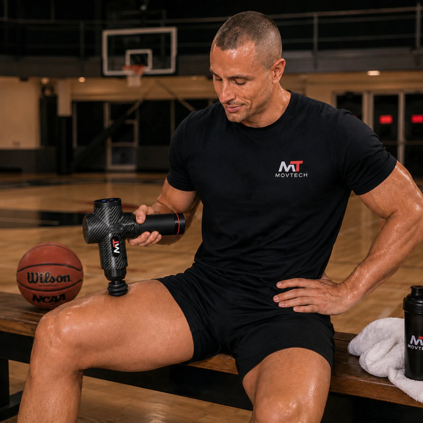 Movtech Elit masszázspisztoly, kosárlabdapályán padon ülő sportoló a saját combizmát kezeli vele