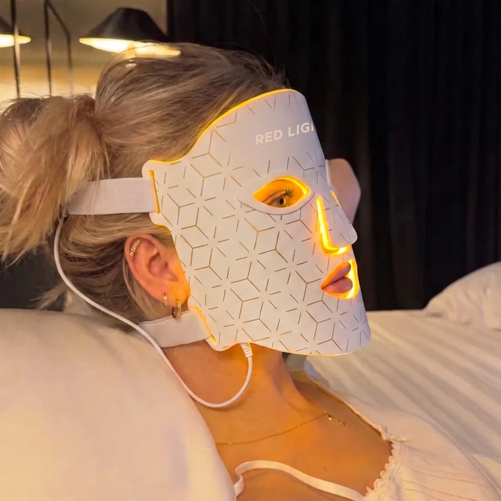 Nő pihen az ágyon a Movtech Red Light Mask LED arcmaszkkal, borostyánsárga fénnyel